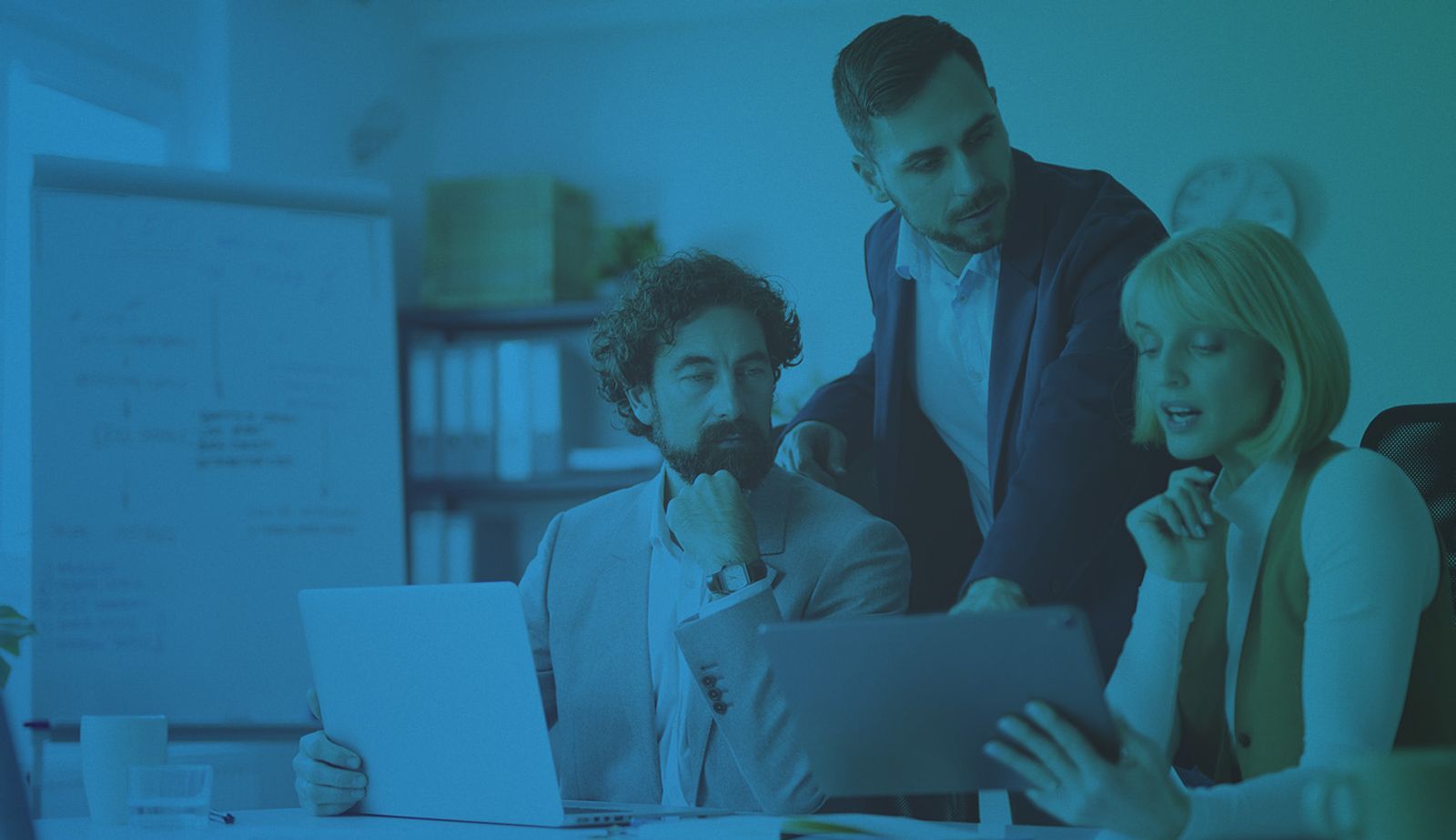 Stock image with an overlay showing three coworkers in an office observing an laptop and a tablet.