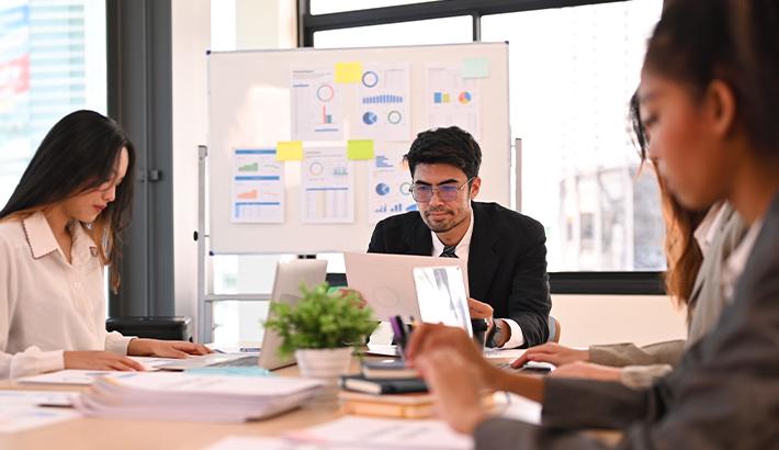 Stock image showing a group of people working in an office with a whiteboard with infographics.