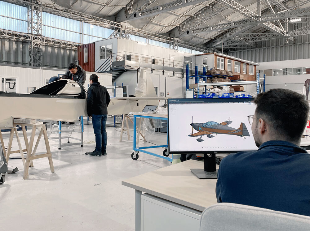 two people working on aircraft in warehouse while another person works on an Onshape model of the aircraft